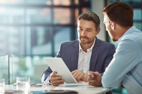 Two professional men in an office reviewing data on a digital tablet, showcasing business consulting and strategic planning.