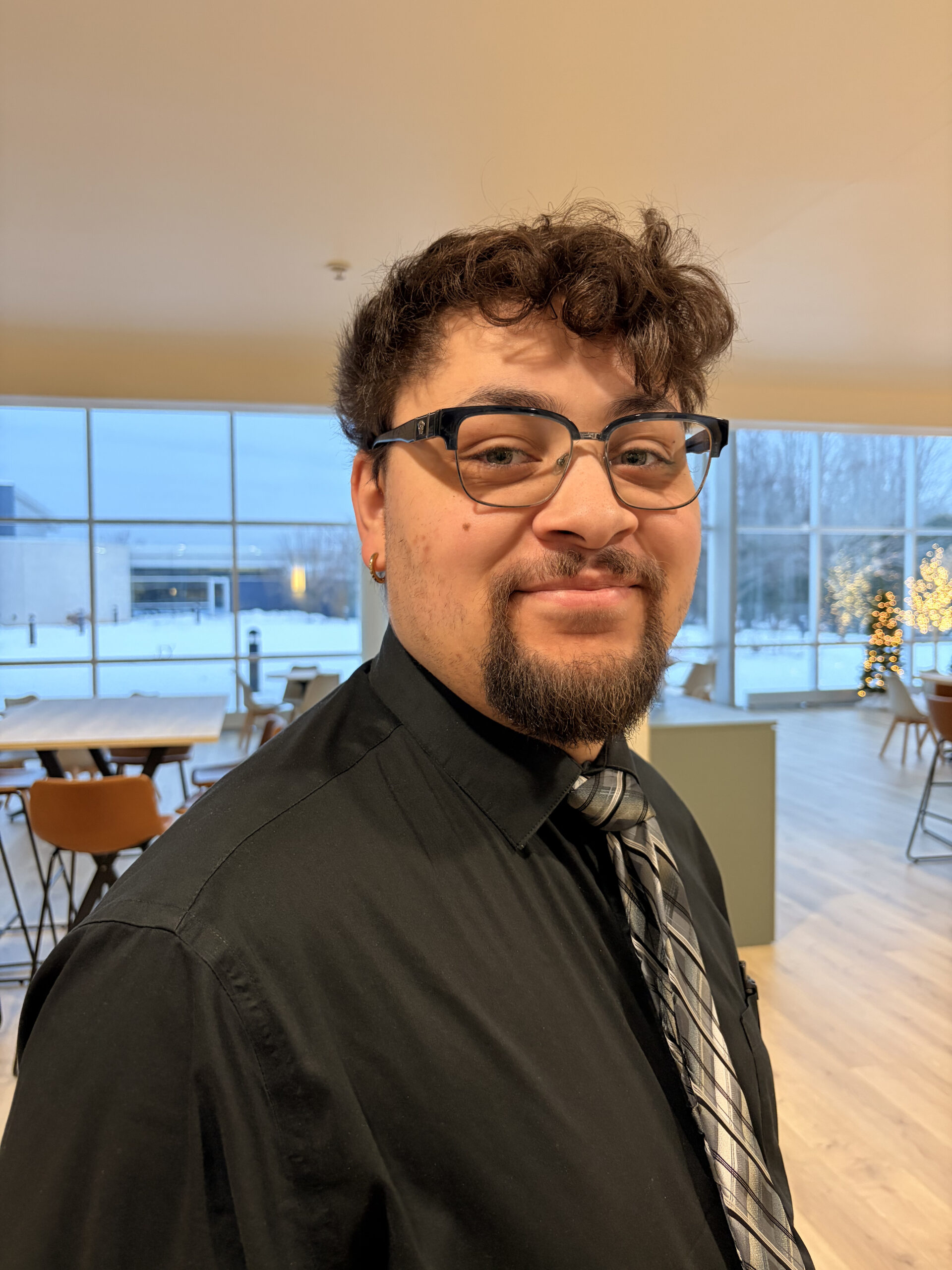 Close-up portrait of a professional man with glasses and a tie in a bright office environment, signifying expertise and corporate leadership.